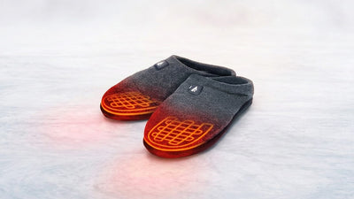 A pair of grey fabric slippers with glowing red heating elements on their front, sitting on a light textured surface.