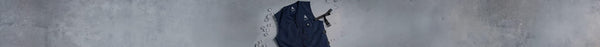 A navy blue zippered cooling vest with a white mountain logo and black strap lies on a gray surface, surrounded by scattered clear ice cubes.