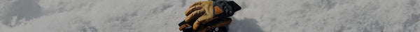A pair of brown leather and black Thinsulate gloves rests on a pristine, textured white snow surface under bright light.