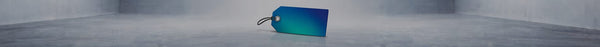 A blue and green gradient price tag with a black string loop lies on a light gray concrete floor in a minimalist room, casting a reflection.