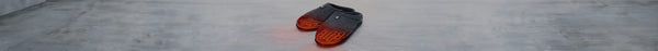 A pair of grey slippers with glowing orange-red patterned soles rests on a light grey floor.