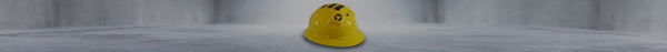 A yellow hard hat with black stripes and a black swirling logo rests upside down on a light grey floor in a blurred room.