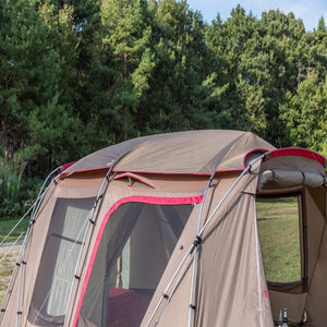 Snow Peak brown and red camping tent set up in a grassy field with trees in the background