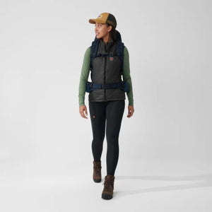 Person wearing FjallRaven vest, long sleeve shirt, leggings, hiking boots, cap, and backpack