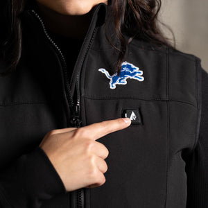 Person pressing the power button on a black ActionHeat Detroit Lions heated vest