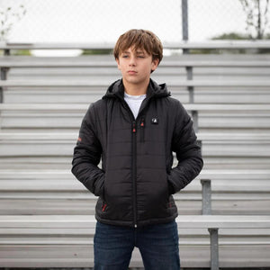 Boy wearing a black ActionHeat hooded heated jacket standing in front of stadium bleachers