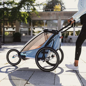 Person pushing a light blue Thule Cross multisport trailer on a paved path