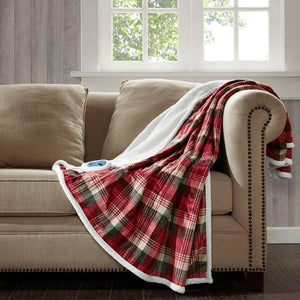 Woolrich red and green plaid heated throw blanket with white sherpa lining draped over a beige sofa