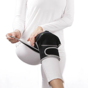Person adjusting a black knee brace with grey trim on their leg