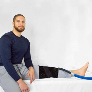 Man wearing a black compression wrap on his knee connected to a blue therapy hose