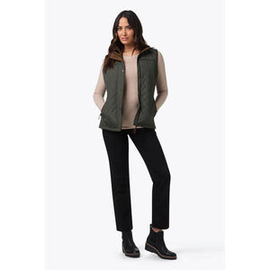 Woman wearing a Mobile Warming olive green quilted vest over a beige long sleeve shirt and black pants