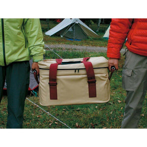 Two people carrying a tan Snow Peak soft cooler bag with red straps at a campsite