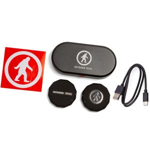 Outdoor Tech charging case with two wireless earbuds, charging cable, and brand sticker