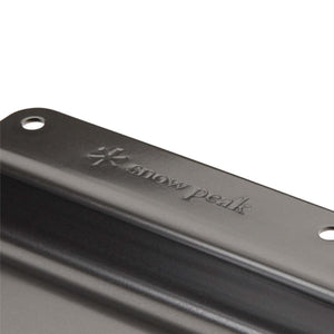 Close up of a black Snow Peak metal component with embossed logo and mounting holes