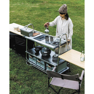 Person using a Snow Peak modular outdoor kitchen setup on a grassy field