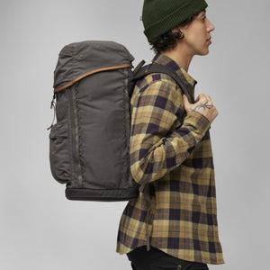 Person wearing a grey FjallRaven backpack with leather trim and a plaid shirt