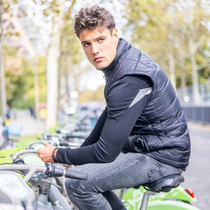 Man wearing a black quilted vest and long sleeve shirt sitting on a green rental bicycle