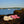 Acorn white and pink plush flip flops on a rocky shore with sailboats in the background