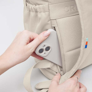 Hand placing a smartphone into the side zipper pocket of a beige backpack