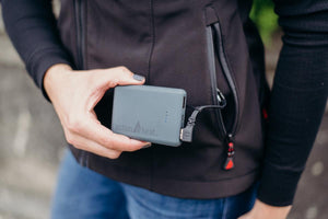 Person holding an ActionHeat power bank connected to a black jacket pocket