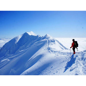 Climber in Dr Warm gear standing on a snow covered mountain ridge above clouds