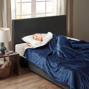 Person sleeping under a navy blue Woolrich heated blanket on a bed