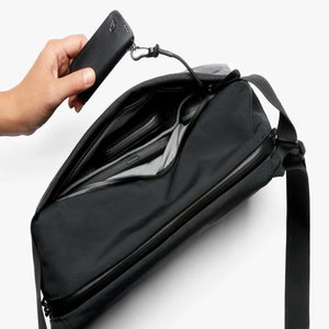 Hand holding a Bellroy key cover attached to a cord inside a black crossbody bag