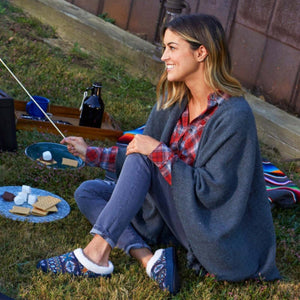 Woman wearing Acorn slippers with patterned fabric and white fleece lining sitting on grass