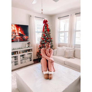 Person wearing Acorn slippers sitting on a coffee table in a living room with a Christmas tree