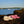 Acorn white and pink plush flip flops on a rock by the water