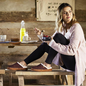 Woman wearing Acorn slippers sitting on a wooden bench eating breakfast