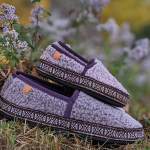 Acorn purple fleece slippers with patterned trim resting on grass