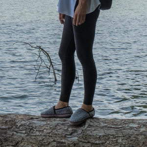 Person wearing Acorn grey fleece slippers standing on a log by the water