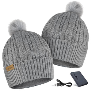 Two grey cable knit ActionHeat beanies with pom poms and a portable battery pack with charging cable