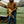 Man wearing ActionHeat brown work jacket putting on yellow leather work gloves by construction equipment