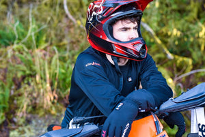 Person wearing ActionHeat black long sleeve shirt and gloves with a red motocross helmet leaning on a dirt bike