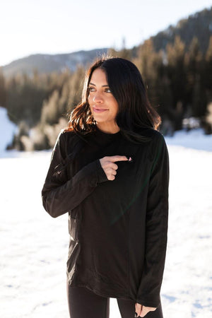 Woman wearing black ActionHeat long sleeve shirt pointing to the power button in a snowy outdoor setting