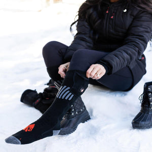 Person wearing black ActionHeat battery heated socks while sitting in snow
