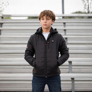 Boy wearing a black ActionHeat hooded puffer jacket standing in front of stadium bleachers