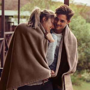 Couple wrapped in an ActionHeat brown fleece blanket on a wooden deck