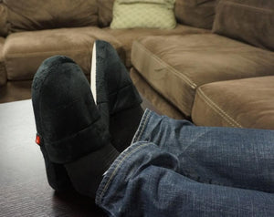 ActionHeat black heated slippers worn on feet resting on a table