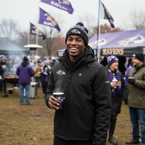 Man wearing ActionHeat black jacket and Baltimore Ravens beanie holding a steaming cup at a tailgate