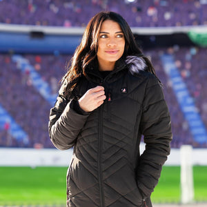 Woman wearing a black quilted heated jacket with a faux fur hood at a stadium