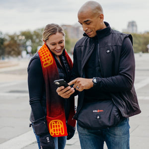 Woman wearing ActionHeat heated scarf and man wearing ActionHeat heated vest looking at a smartphone