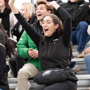 Woman wearing an ActionHeat black vest with Philadelphia Eagles logo cheering in stadium bleachers