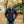 Man wearing a black Aheata zip up jacket and blue jeans standing in a park with autumn leaves