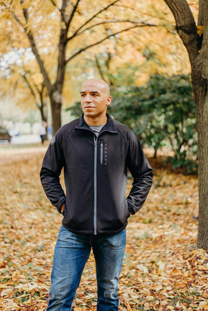 Man wearing a black Aheata zip up jacket and blue jeans standing in a park with autumn leaves