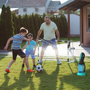 Man and two boys playing soccer on a lawn with a misting fan nearby