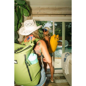 Two women wearing backpacks standing by a sliding glass door looking out at a swimming pool
