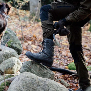 Arctic Volt black leather hiking boot on a rock with a person and dog in a forest